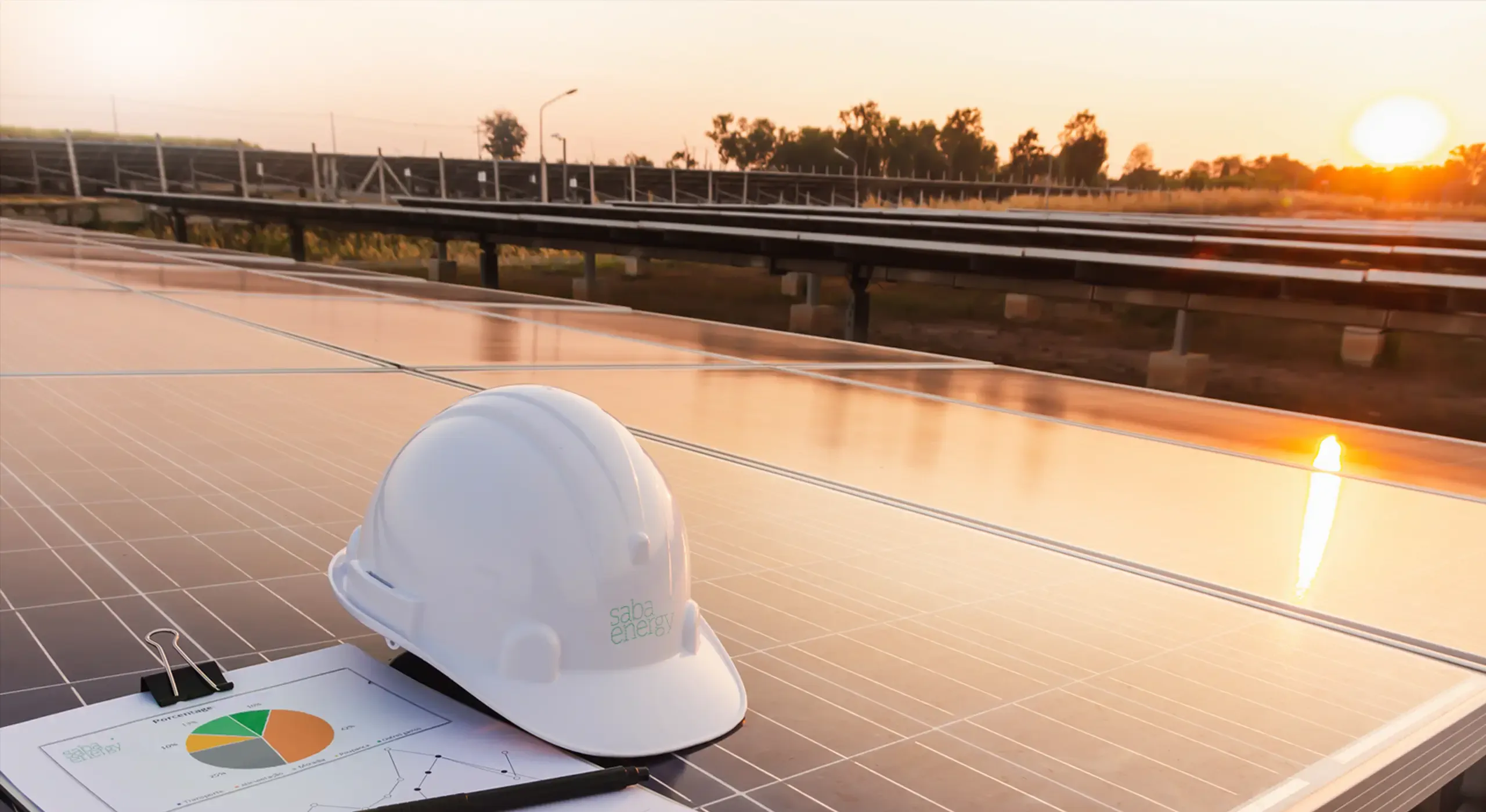 A Saba Energy branded hard hat resting on a solar panel at sunset, with a solar array behind